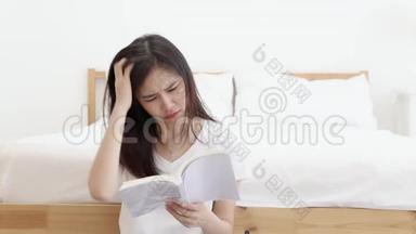 美丽的肖像年轻的亚洲女人坐着看书，在家里的卧室里严肃认真